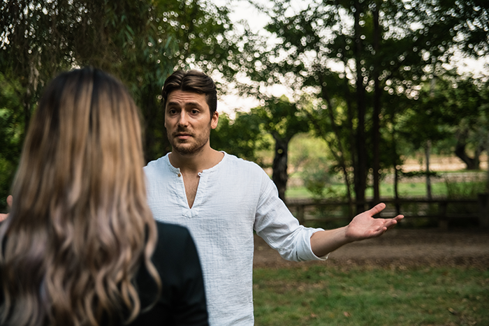 Man expressing frustration outdoors while talking to a woman, illustrating family conflict over a lady kissing another man.