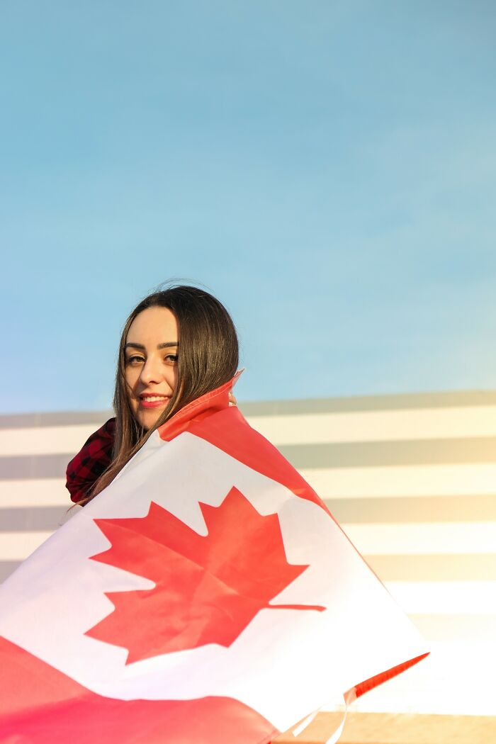 Young woman smiling and wrapped in a Canadian flag representing positive stereotypes about various countries and cultures.