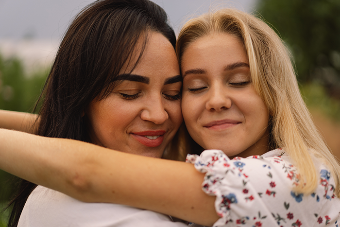 Close-up of a happy clean-f***k mom and daughter sharing an embrace outdoors with eyes closed and content smiles. Close-up of a happy clean-f***k mom and daughter sharing an embrace outdoors with eyes closed and content smiles.