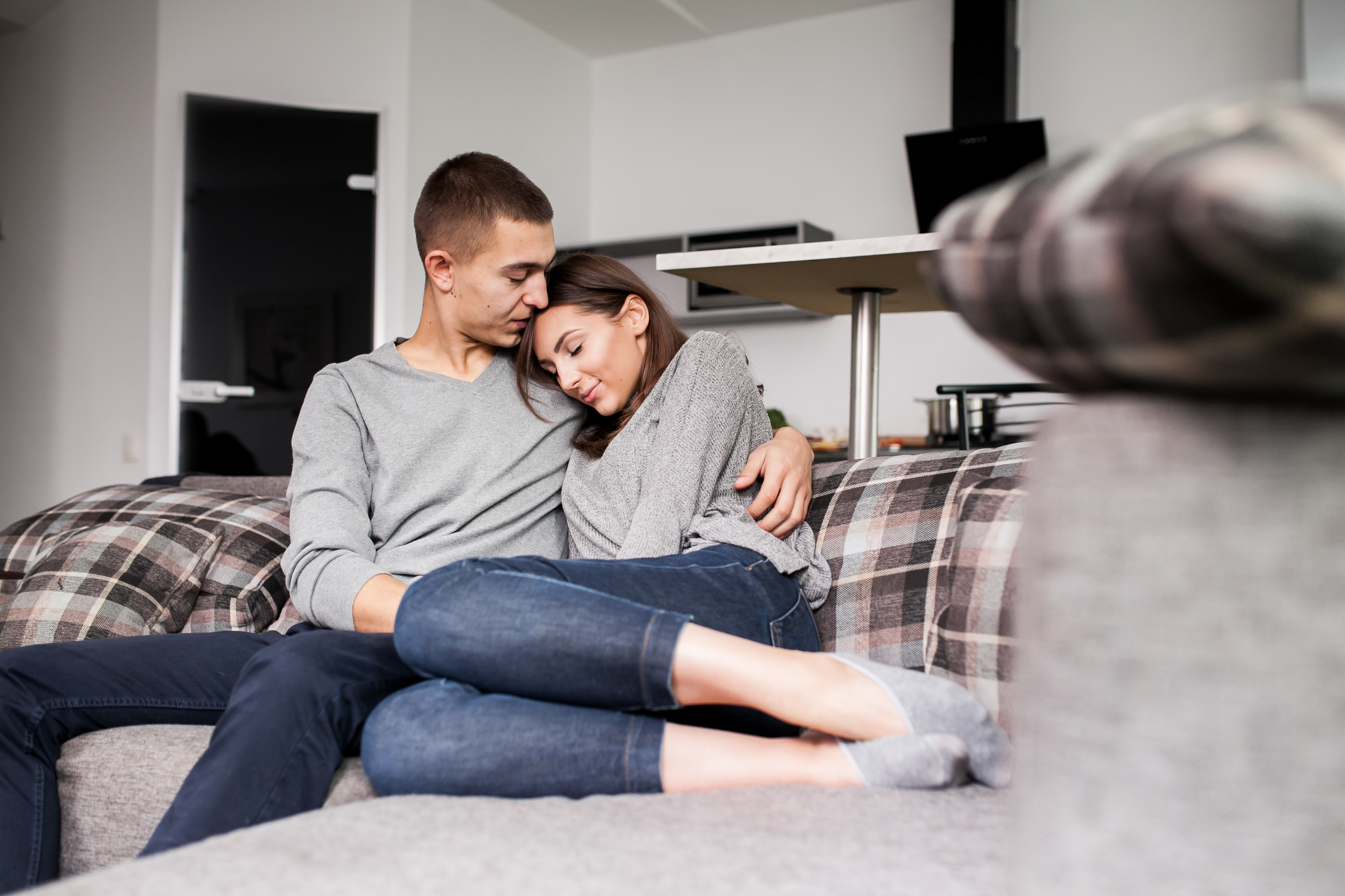 Couple sitting on a plaid couch at home, woman resting on boyfriend while discussing combined income and money issues Couple sitting on a plaid couch at home, woman resting on boyfriend while discussing combined income and money issues