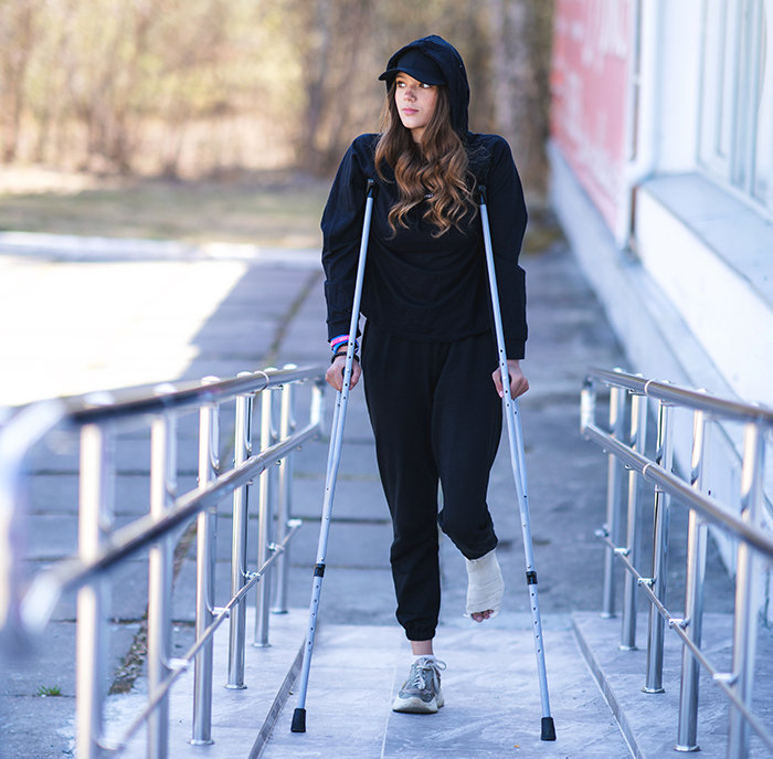 Young woman with injured foot using crutches outdoors, symbolizing mom standing her ground for autistic student’s needs. Young woman with injured foot using crutches outdoors, symbolizing mom standing her ground for autistic student’s needs.