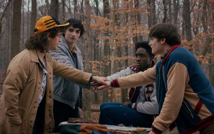 Group of young friends in a forest, linking hands as Stranger Things creators share cryptic warning for fans before final episodes.