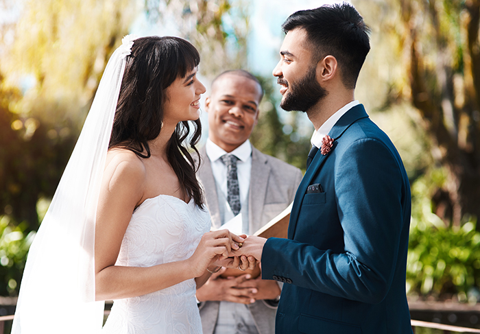 Bride and groom exchanging rings during outdoor wedding ceremony with officiant, capturing spiritual bride’s emotional moment.