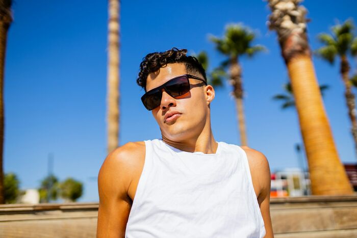 Young man wearing sunglasses and a white sleeveless shirt, reflecting on love and friendship broken by lies and secrets.