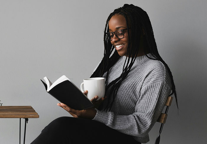 Woman reading romantasy book and holding coffee, reacting to author's controversial comments about readers.