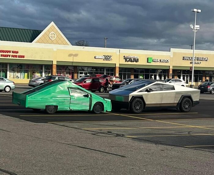 Two unconventional, homemade cars parked side by side in a shopping center parking lot showcasing redneck engineering creativity.