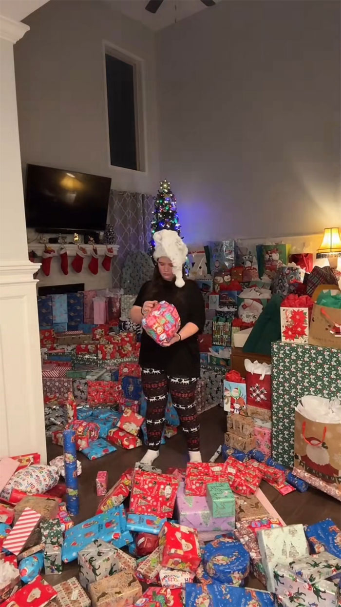 Woman surrounded by an insane amount of gifts in a living room, highlighting consumerism and holiday excess.