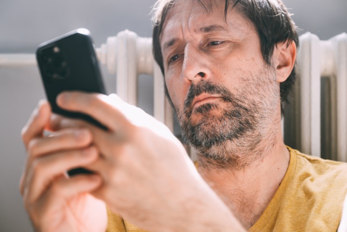Middle-aged man looking upset while holding smartphone, reflecting on husband refusing intimacy for five years.