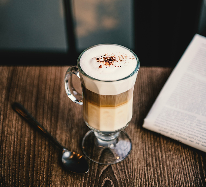 Glass of morning coffee with foam and chocolate sprinkles on a wooden table next to a newspaper and spoon Glass of morning coffee with foam and chocolate sprinkles on a wooden table next to a newspaper and spoon