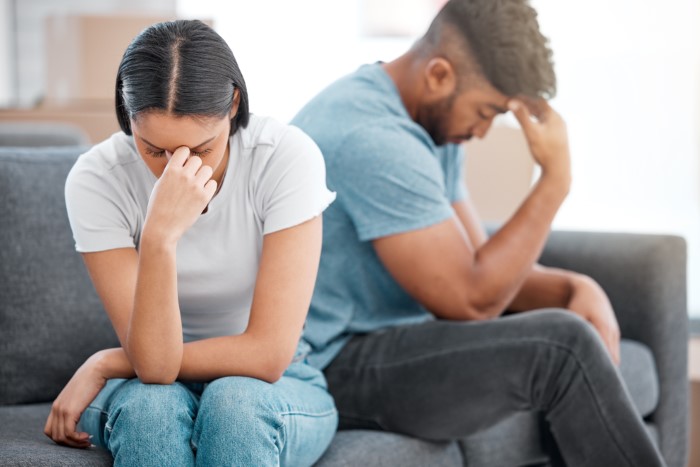 Man and woman sitting apart on sofa, both appearing stressed and upset, highlighting family and work conflict.