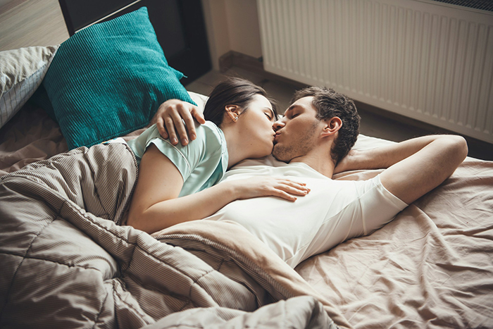 Couple lying in bed kissing closely, representing themes of boyfriend open relationship and relationship dynamics.