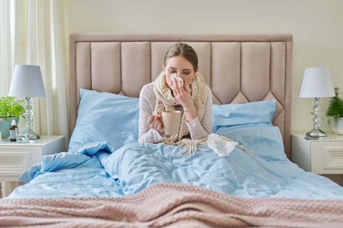 Sick woman in bed holding a cup, symbolizing emotional strain as man prioritizes work over family life.