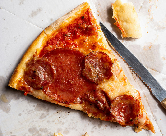 Slice of pepperoni pizza with a bite taken, showing a glimpse of instant karma in a casual eating setting.