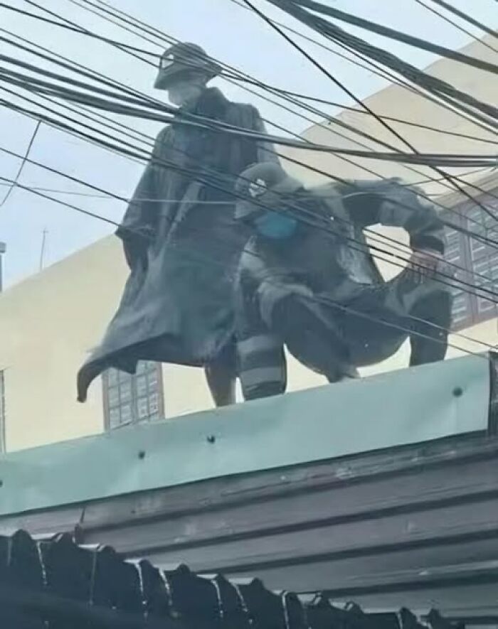 Two statues wearing face masks stand on a rooftop surrounded by overhead wires in a city setting, pics that go hard.