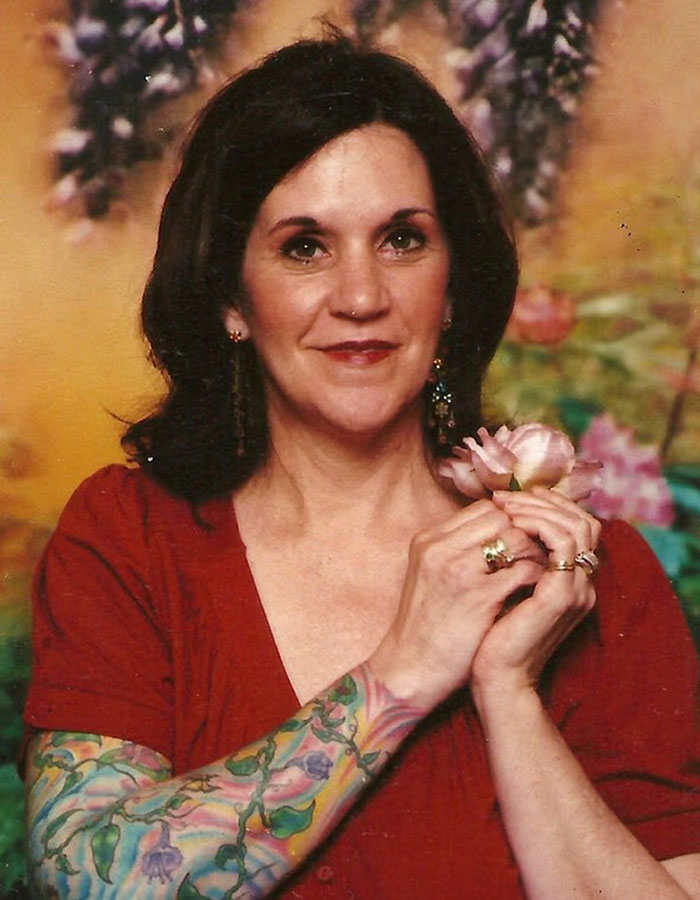 Woman with floral tattoo sleeve holding a pink flower, representing missing woman’s body discovered in garage case.