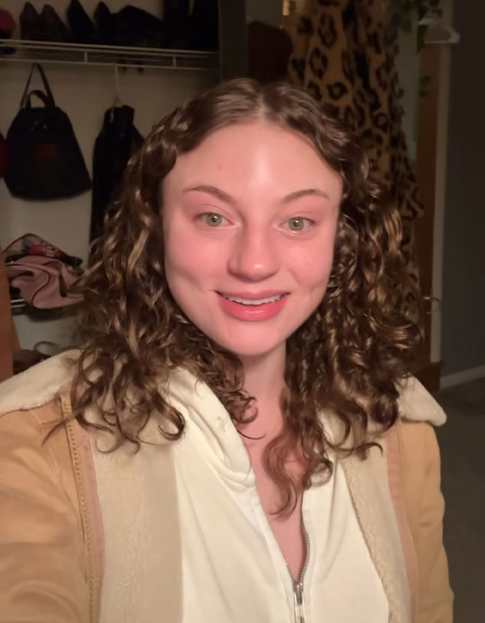 Young woman with curly hair smiling indoors, related to DoorDash driver arrested after recording undressed customer video.