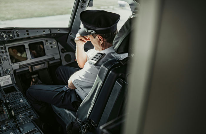 Pilot in uniform sitting in airplane cockpit, appearing stressed, illustrating terrifying close calls mid-flight experiences.