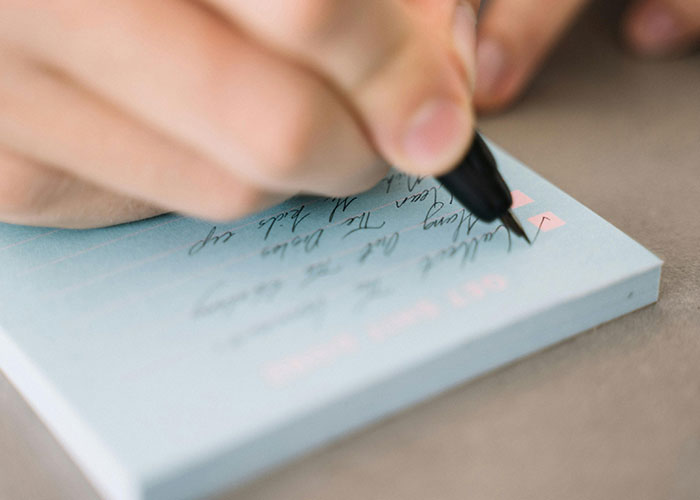 Close-up of a person writing on a notepad, illustrating people sharing life hacks for everyday use.