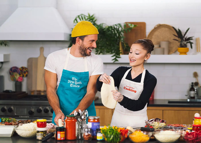 Ariana Grande and Jonathan Bailey sharing a lighthearted moment while preparing food in a modern kitchen. Ariana Grande and Jonathan Bailey sharing a lighthearted moment while preparing food in a modern kitchen.