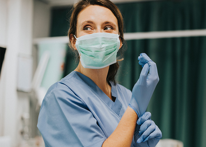 Female nurse wearing mask and blue scrubs preparing gloves in hospital, related to creepy cases doctors and nurses recall.