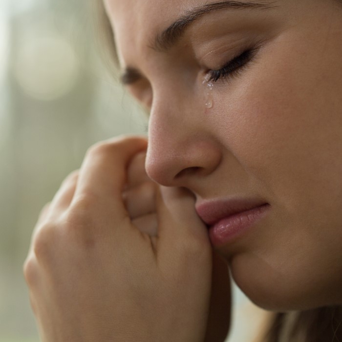 Close-up of a woman crying with tears on her cheek, reflecting emotional pain over family and work priorities.