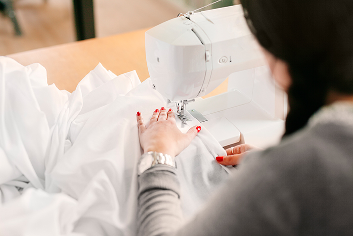 Woman using a sewing machine to remake a wedding dress fabric, highlighting the wedding dress remake process.