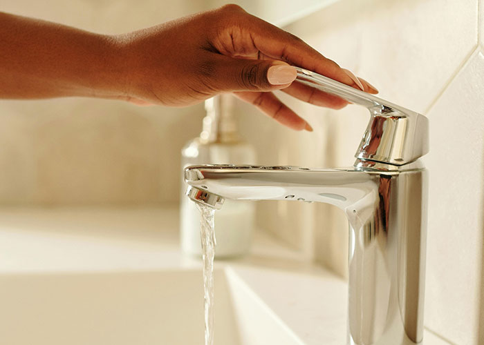 Hand turning on modern faucet with running water in a clean bathroom, illustrating lazy genius cleaning hacks.