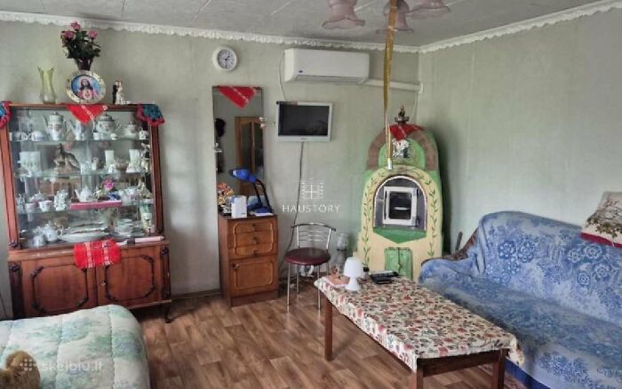 Cozy vintage living room with floral sofa, wood stove, antique china cabinet, and patterned table in real estate listing.