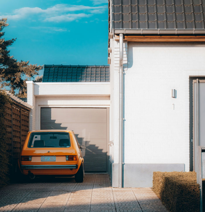 Orange car parked in driveway beside a white house, illustrating common issues with restrictive HOA rules.