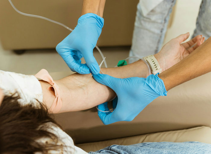 Medical professional wearing blue gloves inserting IV needle in patient's arm, capturing funny patients comments in clinics and hospitals.