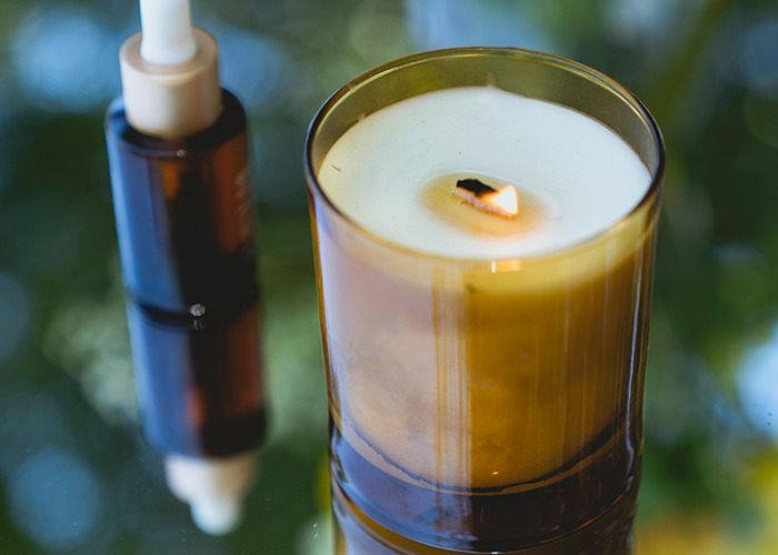 Lit scented candle and brown dropper bottle on reflective surface, representing horrible gifts people have received.