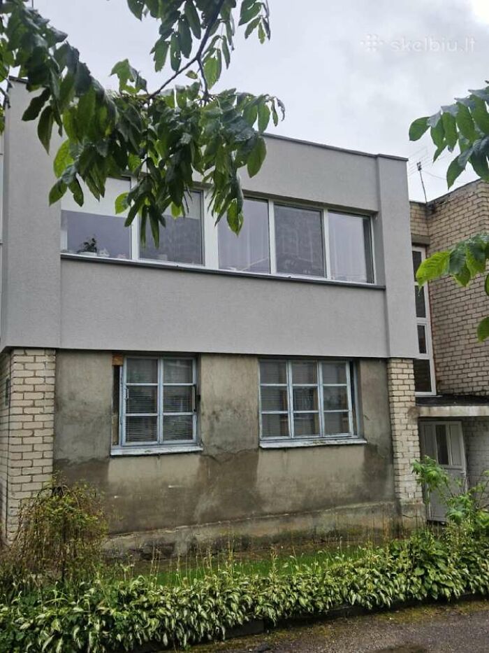 Two-story real estate listing showing mismatched window designs and uneven exterior wall finishes with greenery in front.