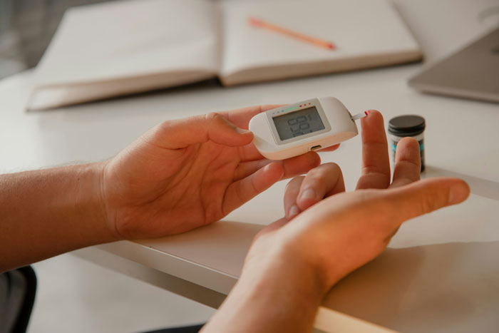 Person checking blood sugar level with glucometer at a desk, illustrating consequences of eating what one shouldn’t. Person checking blood sugar level with glucometer at a desk, illustrating consequences of eating what one shouldn’t.