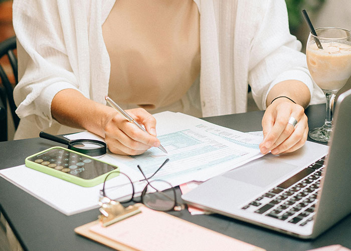 Person writing notes and using laptop with calculator and glasses nearby, focusing on common knowledge insights.