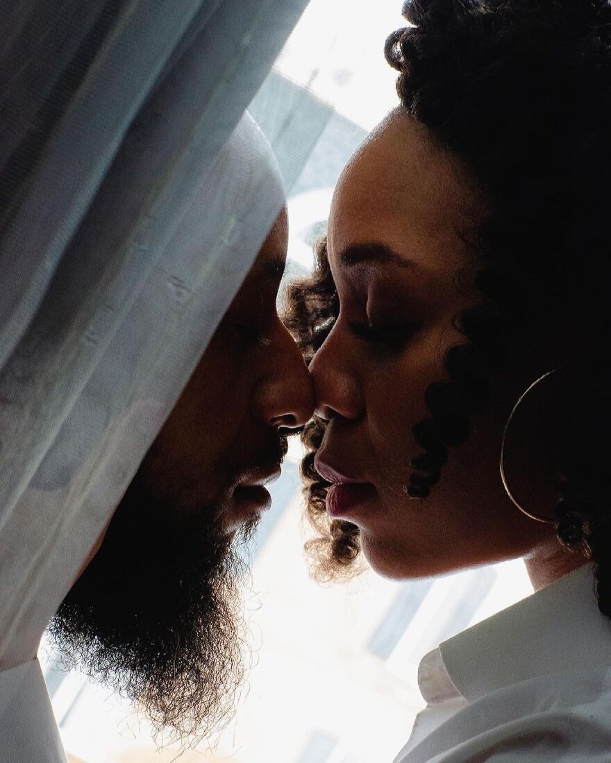 Couple sharing an intimate moment close to a window, illustrating different types of kisses in culture and history.
