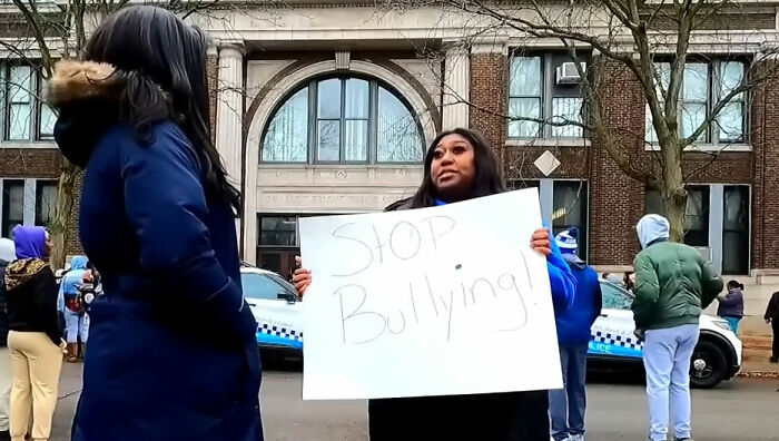 Woman holding stop bullying sign outside school after pregnant woman attacked by mob of young school kids Woman holding stop bullying sign outside school after pregnant woman attacked by mob of young school kids