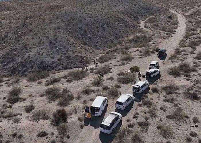 Aerial view of multiple white vans and people gathered on a dirt road in a desert area near Las Vegas museum. Aerial view of multiple white vans and people gathered on a dirt road in a desert area near Las Vegas museum.