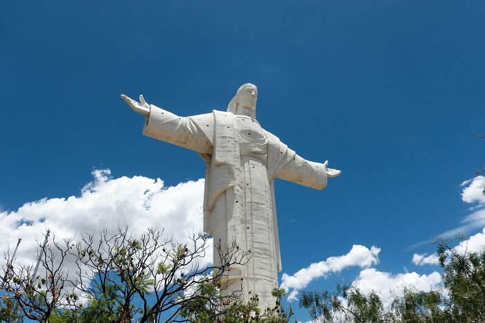Large white sculpture of a figure with outstretched arms under a blue sky, a must-see spectacular sculpture for travel.