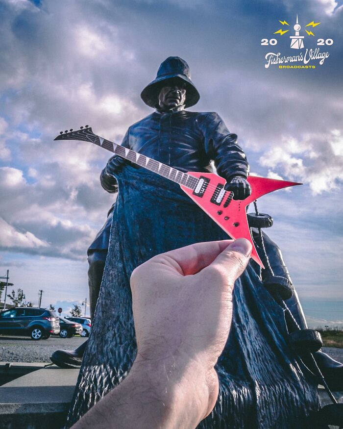 Hand holding a paper cutout guitar interacting with a statue, showcasing creative paper cutouts by Rudy Willingham.