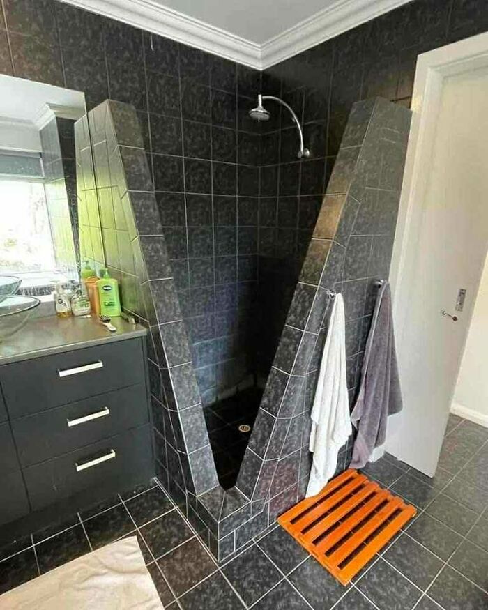 Unusual bathroom shower with dark tiles and a unique V-shaped design in wild real estate listings.