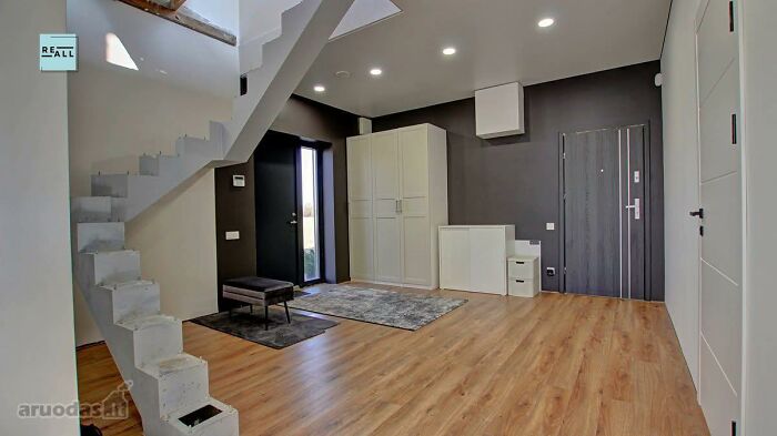 Modern empty real estate listing interior with wooden flooring, minimalist staircase, and storage cabinets in a bright room.
