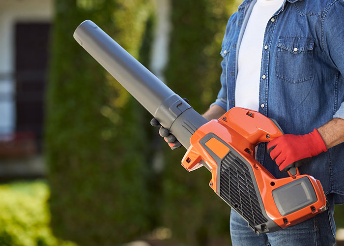 Person wearing red gloves holding an orange leaf blower demonstrating genius cleaning hacks inspired by laziness outdoors.