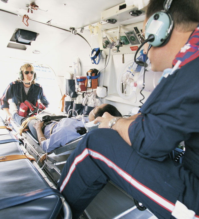 Two paramedics attending a patient on a stretcher inside an ambulance, illustrating hospital and clinic scenes.