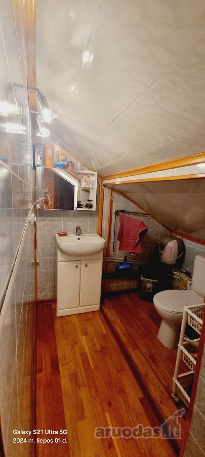 Small attic bathroom with sloped ceiling, wooden floor, white sink cabinet, toilet, and towel hanging on rack.