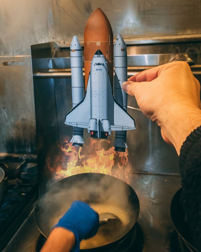 Hand holding a paper cutout of a space shuttle with flames, interacting with real life kitchen fire and cooking. Hand holding a paper cutout of a space shuttle with flames, interacting with real life kitchen fire and cooking.