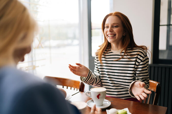 A young woman smiling and talking over coffee, illustrating signs a child was never loved properly through her open expression.