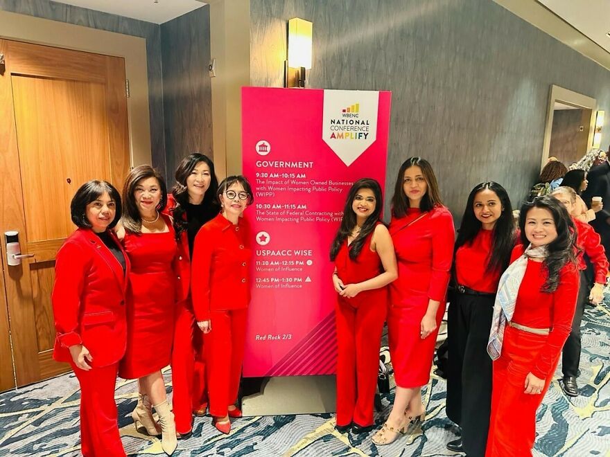 Group of Asian women dressed in red standing by government conference sign, highlighting the fight against Asian stereotypes in modern world.