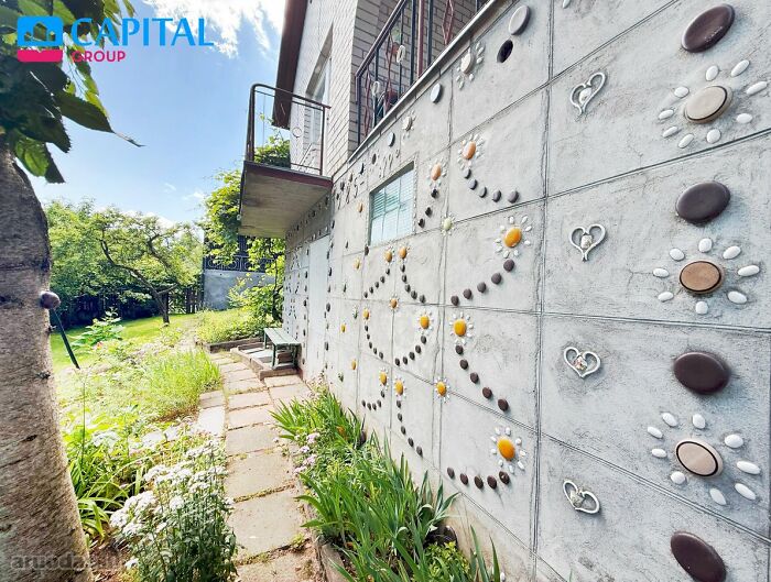 Colorful decorative elements on a modern concrete wall in a wild real estate listing garden pathway setting.