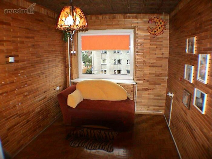Small wooden room with a brown sofa, orange window blind, hanging lamp, and framed pictures on the wall in real estate listing.