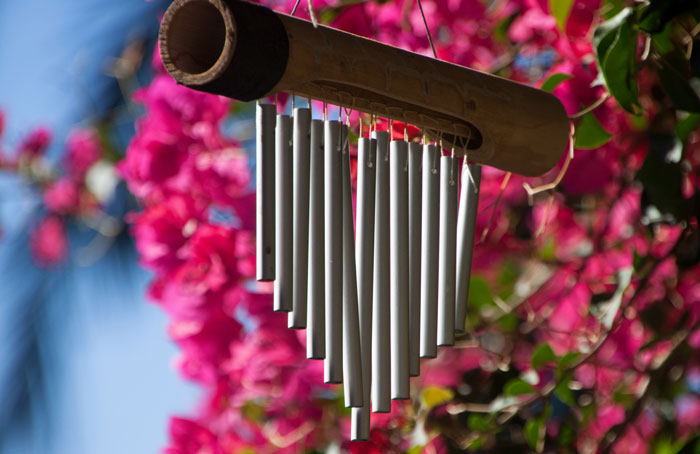 Bamboo wind chime hanging outdoors with bright pink flowers in background illustrating HOA rules on noise and decor complaints.